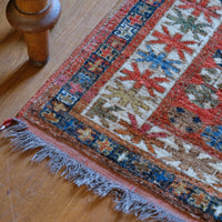 Colorful patterned rug on a wooden floor with a wooden leg partially visible.