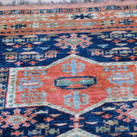 Kazak wool rug with shield kazak medallions - Close-up of a patterned rug with geometric designs in red, blue, and beige.