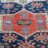 Kazak wool rug with shield kazak medallions - Close-up of a patterned rug with geometric designs in red, blue, and beige.