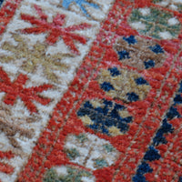 Kazak wool rug with shield kazak medallions - Close-up of a colorful patterned fabric with red, blue, and beige colors.
