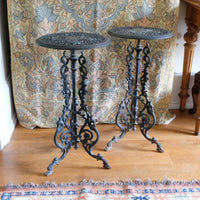 Two ornate metal side tables with intricate designs on a wooden floor.