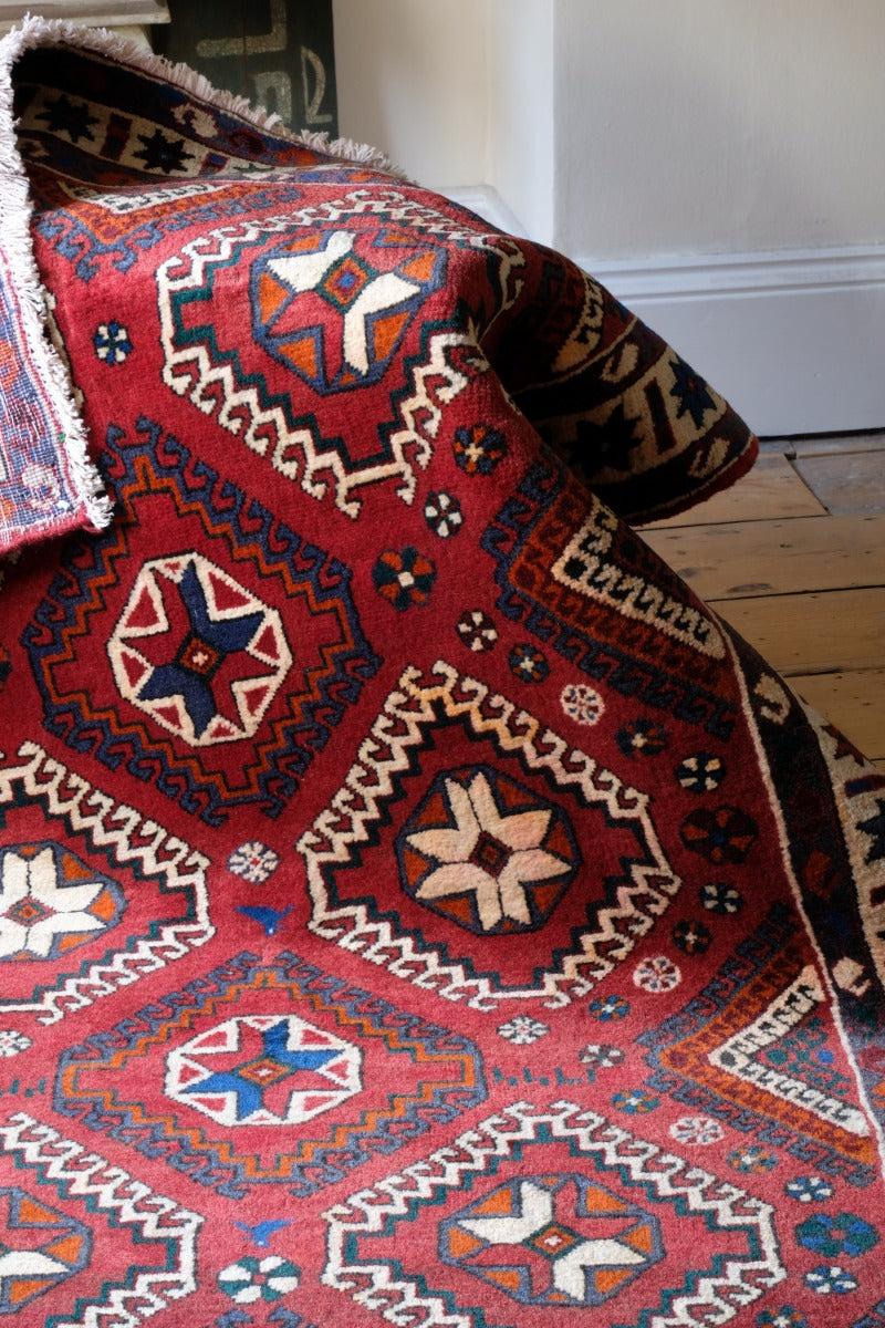 A vintage woolen Kelim rug with a rich red background and vibrant geometric patterns, including stars and medallions, displayed partially folded.