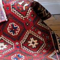 A vintage woolen Kelim rug with a rich red background and vibrant geometric patterns, including stars and medallions, displayed partially folded.