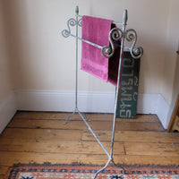 Towel hanging on Early 20th century wrought iron freestanding towel rail with scroll ends and aged painted finish