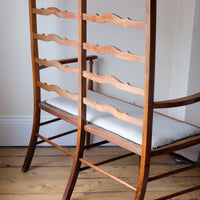 Back view of a 19th century English beech ladder-back bench with linen upholstered horsehair seat and waved slats