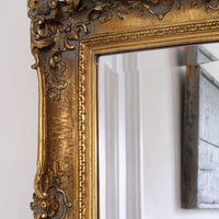 Close up corner view of a Late Victorian gilt wall mirror with original bevelled mirror plate and cherub shelf detail