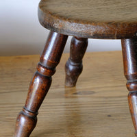 Close up of the natural tseat and painted legs on an Antique English dairy milking stool with four turned legs and original dark painted finish