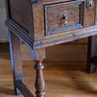 Corner view of the 18th century country oak side table with a single panelled drawer, brass handles and baluster-turned front legs