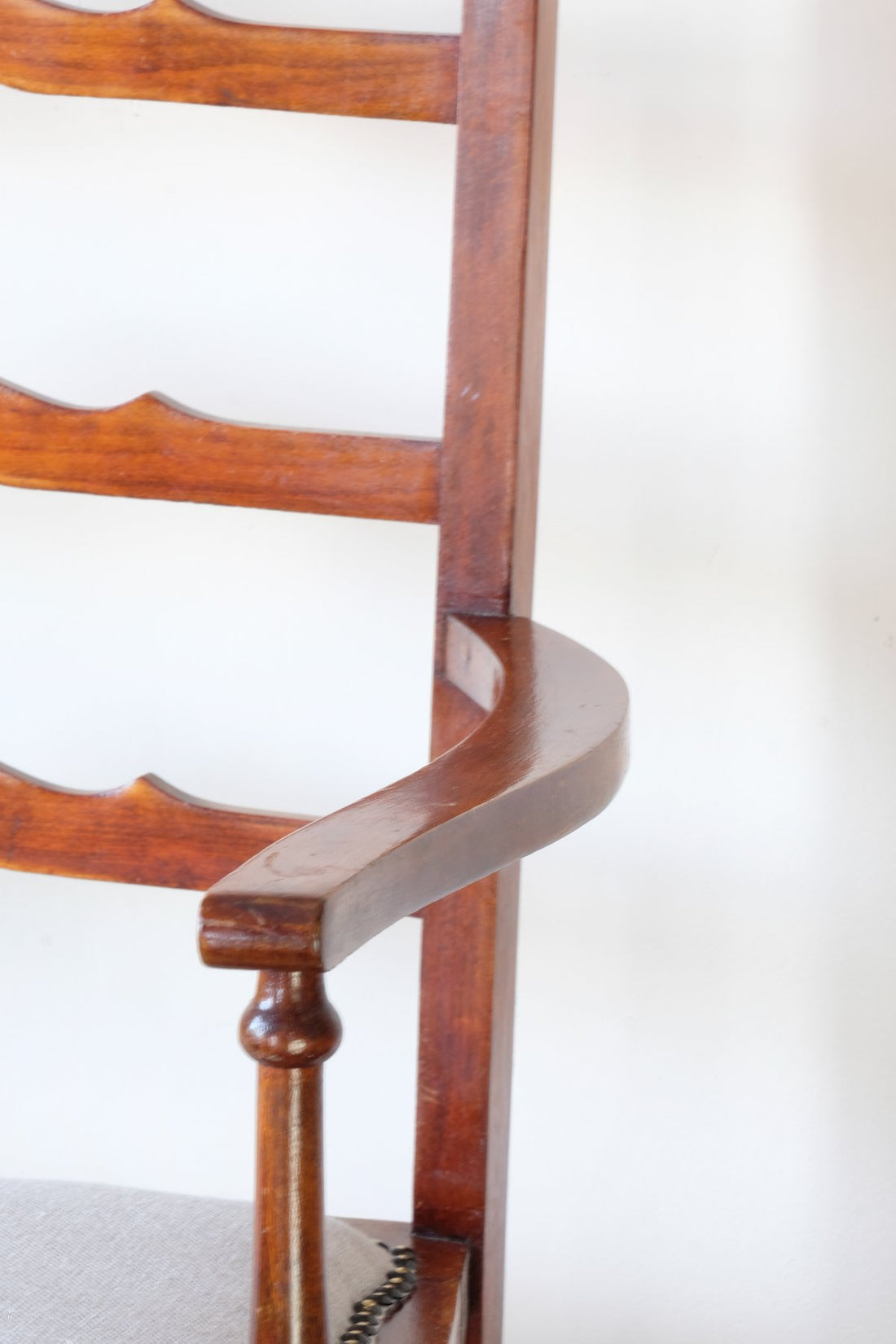 Close up of the serpentine arm - 19th century English beech ladder-back bench with linen upholstered horsehair seat and waved slats
