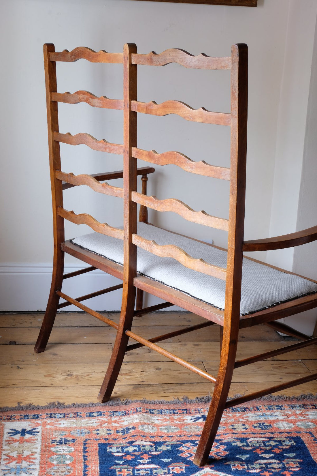 Back view of a 19th century English beech ladder-back bench with linen upholstered horsehair seat and waved slats