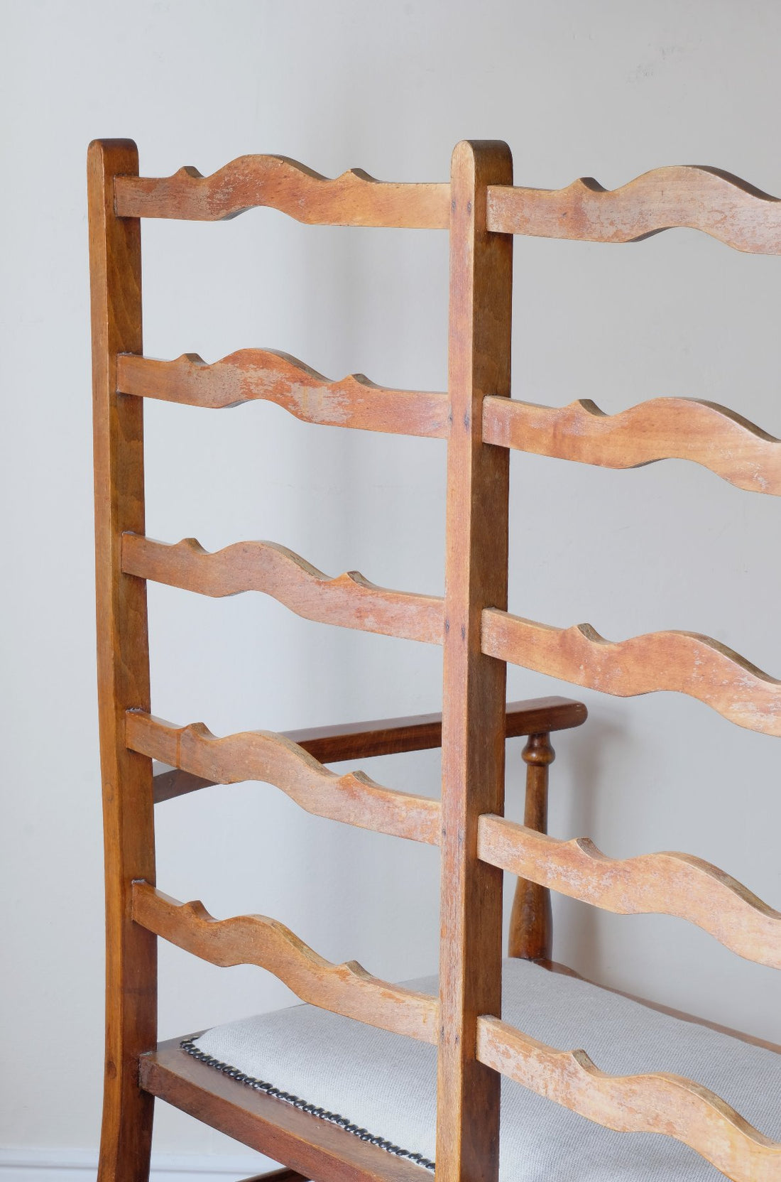 Close up back view of a 19th century English beech ladder-back bench with linen upholstered horsehair seat and waved slats