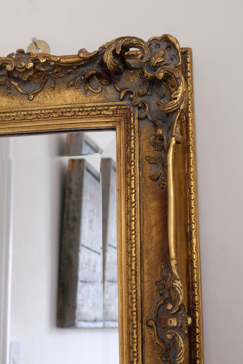 Close up corner view of a Late Victorian gilt wall mirror with original bevelled mirror plate and cherub shelf detail