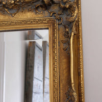 Close up corner view of a Late Victorian gilt wall mirror with original bevelled mirror plate and cherub shelf detail