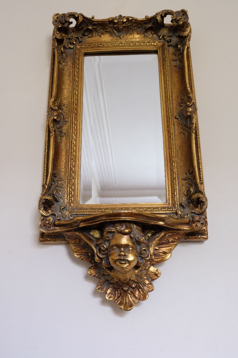 Upward view of a Close up corner view of a Late Victorian gilt wall mirror with original bevelled mirror plate and cherub shelf detail