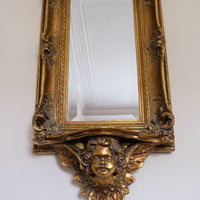 Upward view of a Close up corner view of a Late Victorian gilt wall mirror with original bevelled mirror plate and cherub shelf detail