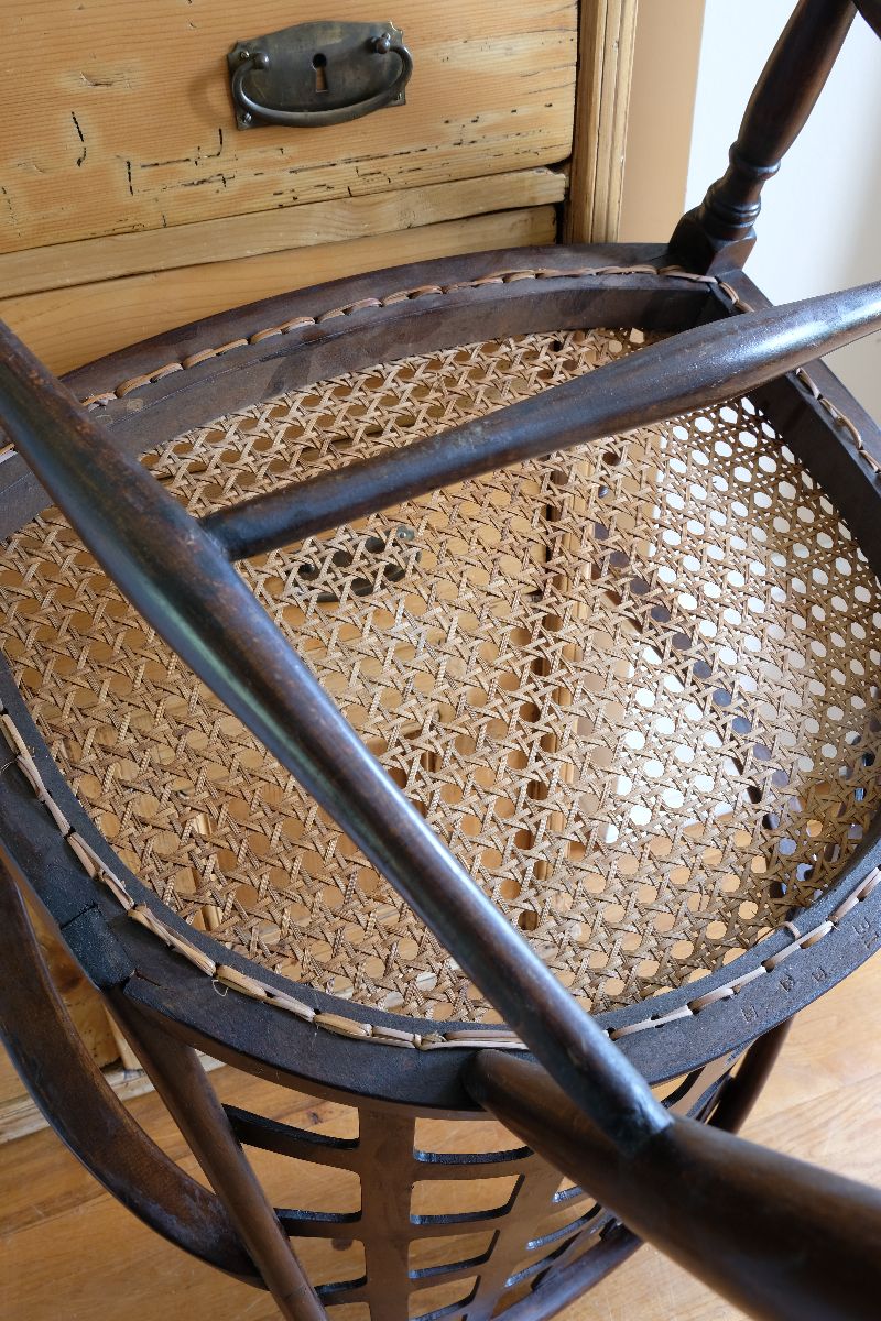 Underneath of a View of the cane seat on a Rare Edwardian bentwood lattice back armchair attributed to Jas Shoolbred with pierced Arts & Crafts design 