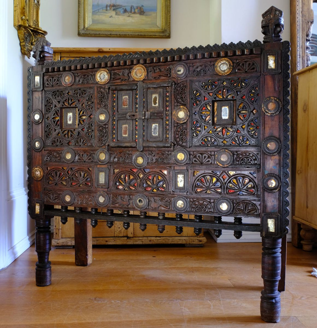 The light captures the reflective mirror, gilt , red and gold ochre colours on this Antique Kutch Damchiya dowry chest with mirror inlay and carved hardwood fretwork, Gujarat c.1900–1930