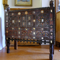 The light captures the reflective mirror, gilt , red and gold ochre colours on this Antique Kutch Damchiya dowry chest with mirror inlay and carved hardwood fretwork, Gujarat c.1900–1930