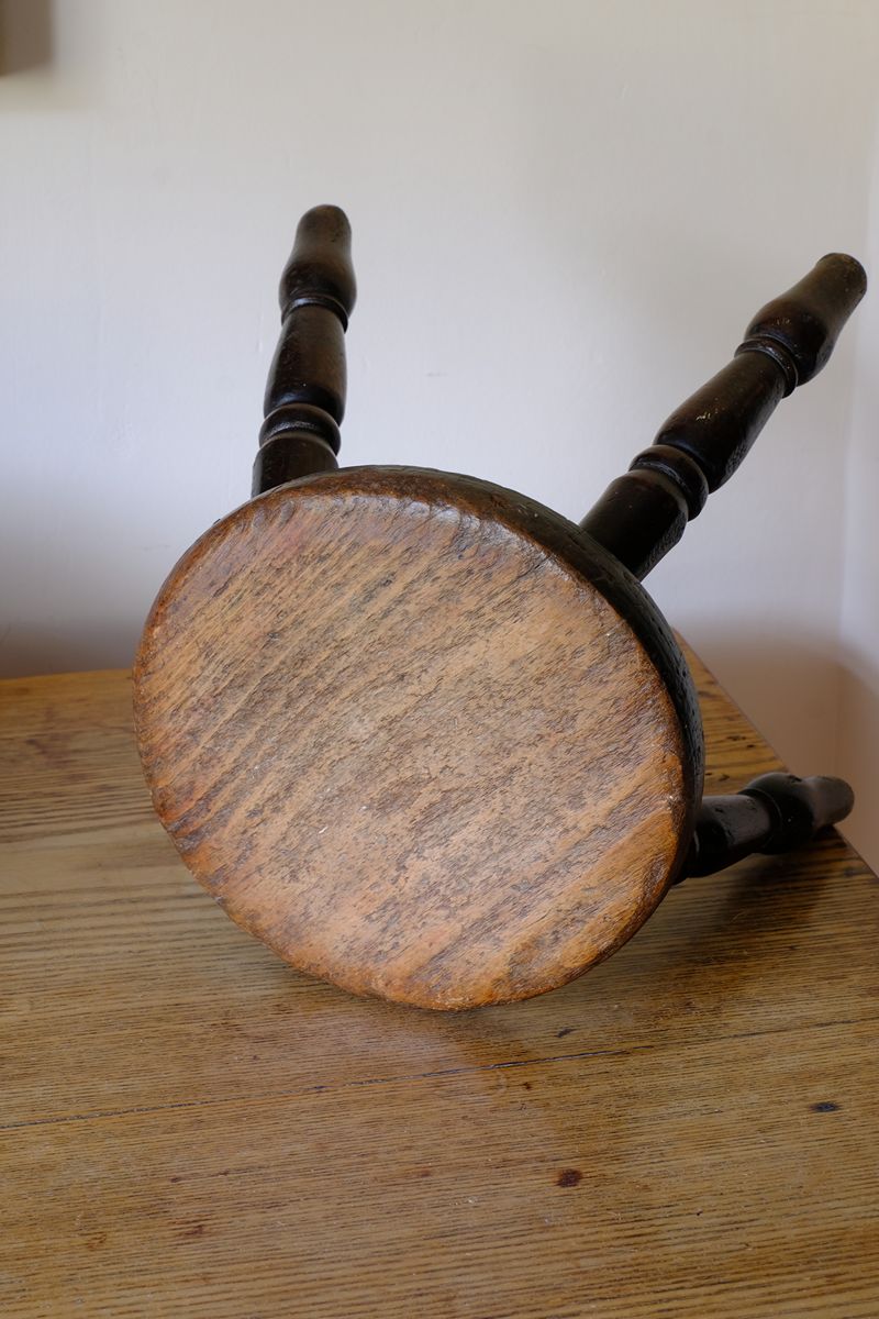 Full view of the top of the seat on an Antique English dairy milking stool with four turned legs and original dark painted finish
