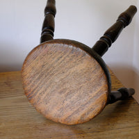 Full view of the top of the seat on an Antique English dairy milking stool with four turned legs and original dark painted finish