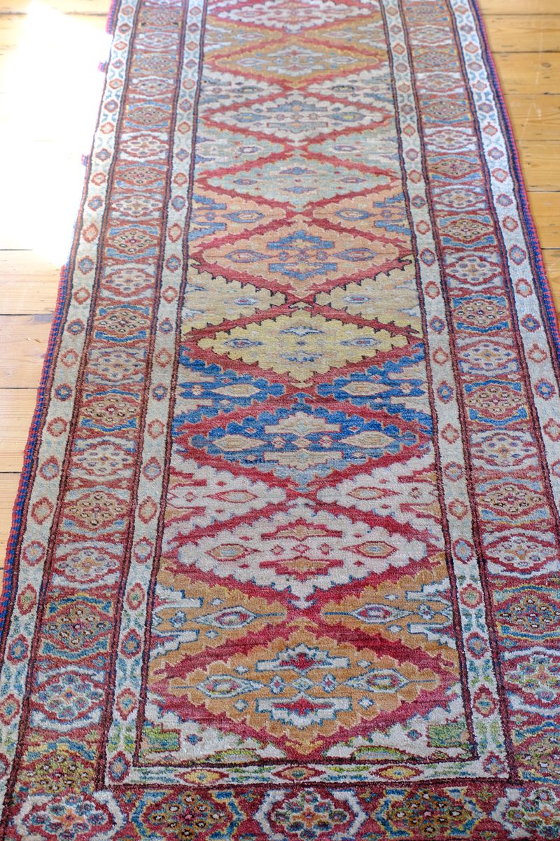 Harmony of colours throughout the Mid-20th Century North-West Persian ivory ground hand-knotted wool runner with fourteen hooked lozenge medallions