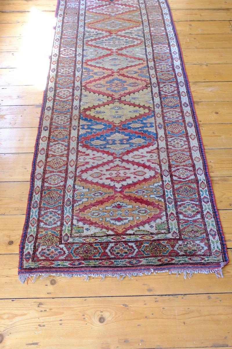 Tasselled ned of the Mid-20th Century North-West Persian ivory ground hand-knotted wool runner with fourteen hooked lozenge medallions