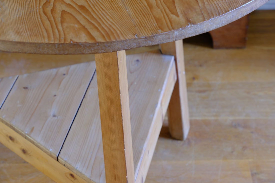 The three splayed legs are particularly well considered, each worked to an unusual faceted profile with a pronounced V-shaped front and softened chamfered rear, creating an irregular lozenge-like section. The changing planes catch the light and visually lighten the structure while retaining the timber required for the substantial pegged joints.