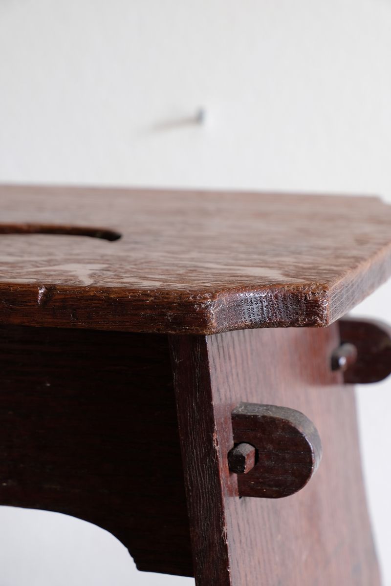 Projecting through-tenons secured by shaped wooden keys on this Antique Arts and Crafts oak low stool with S-shaped carrying handle, fret-cut arches and exposed keyed through-tenons, circa 1900.
