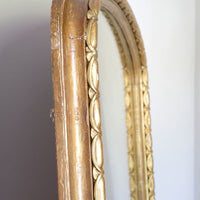 The frame itself has a substantial architectural section, built around a broad convex cushion-moulded outer profile. Set immediately inside this is the continuous carved guilloche-derived border of elongated oval reserves, followed by a restrained inner moulding framing the original arched plate. Seen from the side, the depth of these successive mouldings becomes particularly apparent, giving the mirror considerably more sculptural presence than its relatively restrained frontal outline initially suggests.