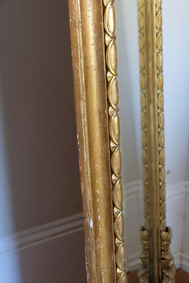 The frame itself has a substantial architectural section, built around a broad convex cushion-moulded outer profile. Set immediately inside this is the continuous carved guilloche-derived border of elongated oval reserves, followed by a restrained inner moulding framing the original arched plate. Seen from the side, the depth of these successive mouldings becomes particularly apparent, giving the mirror considerably more sculptural presence than its relatively restrained frontal outline initially suggests.