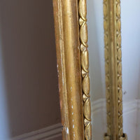 The frame itself has a substantial architectural section, built around a broad convex cushion-moulded outer profile. Set immediately inside this is the continuous carved guilloche-derived border of elongated oval reserves, followed by a restrained inner moulding framing the original arched plate. Seen from the side, the depth of these successive mouldings becomes particularly apparent, giving the mirror considerably more sculptural presence than its relatively restrained frontal outline initially suggests.