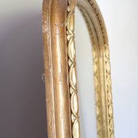 The frame itself has a substantial architectural section, built around a broad convex cushion-moulded outer profile. Set immediately inside this is the continuous carved guilloche-derived border of elongated oval reserves, followed by a restrained inner moulding framing the original arched plate. Seen from the side, the depth of these successive mouldings becomes particularly apparent, giving the mirror considerably more sculptural presence than its relatively restrained frontal outline initially suggests.