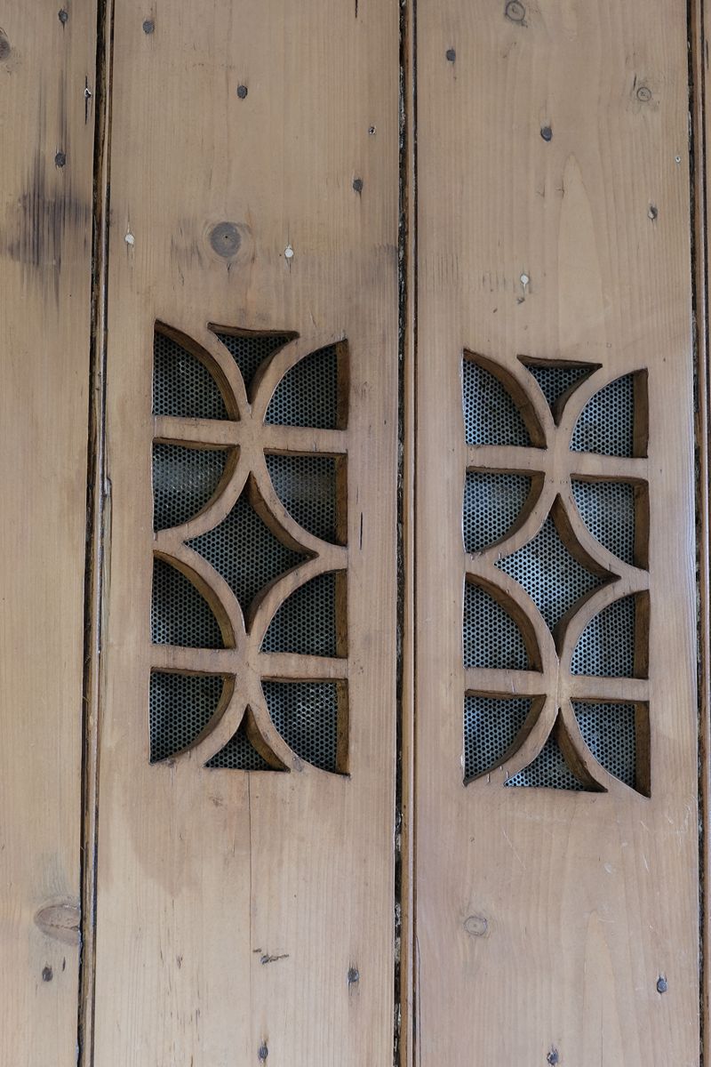 close up of the fret work tracery on the Antique pine cupboard, circa 1890–1910, with a boarded door, two pierced ventilation panels and a plinth base