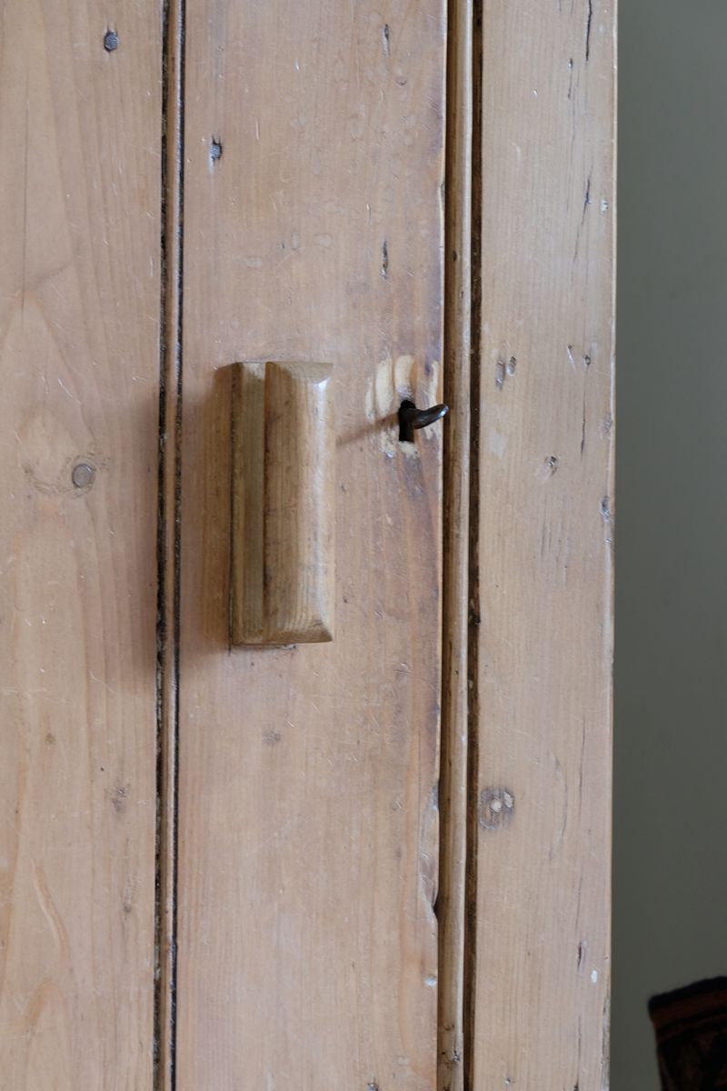 close up of the shaped wooden handle - Antique pine cupboard, circa 1890–1910, with a boarded door, two pierced ventilation panels and a plinth base