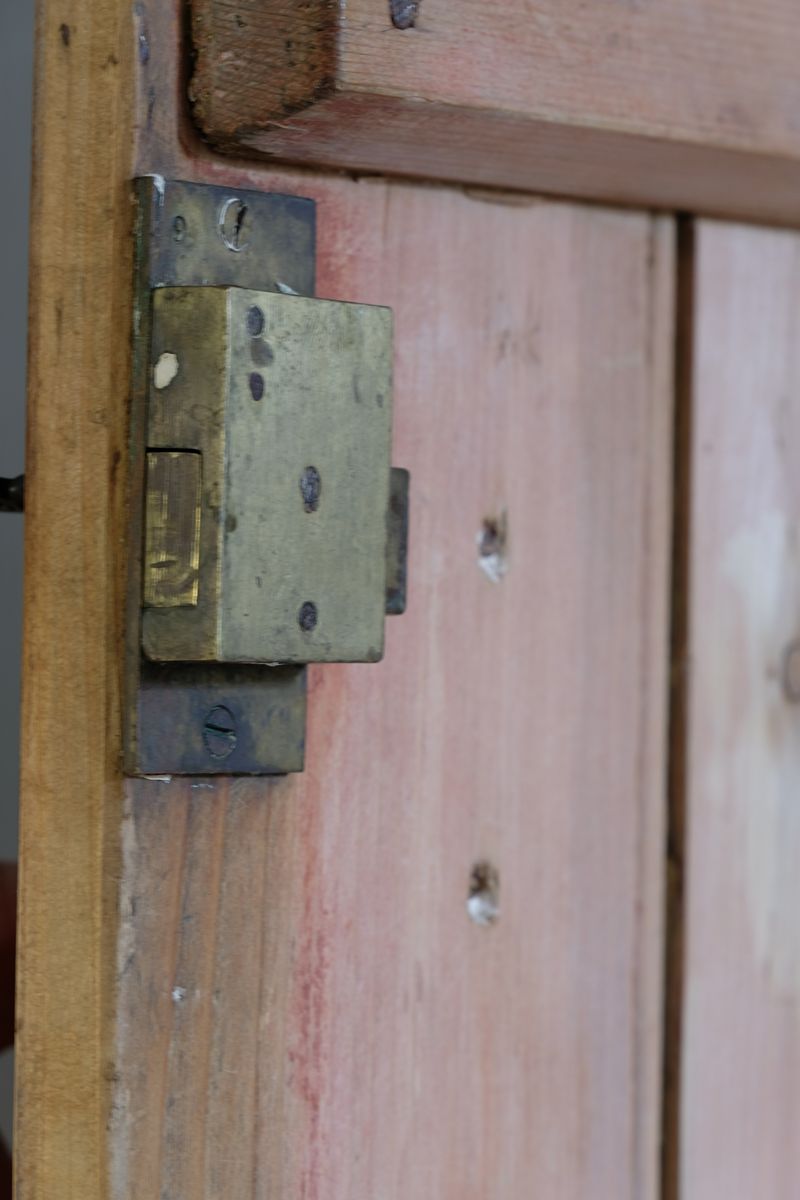 close up of the working lock on the Antique pine cupboard, circa 1890–1910, with a boarded door, two pierced ventilation panels and a plinth base