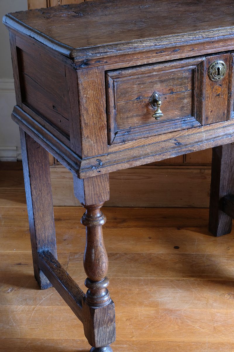 Corner view of the 18th century country oak side table with a single panelled drawer, brass handles and baluster-turned front legs