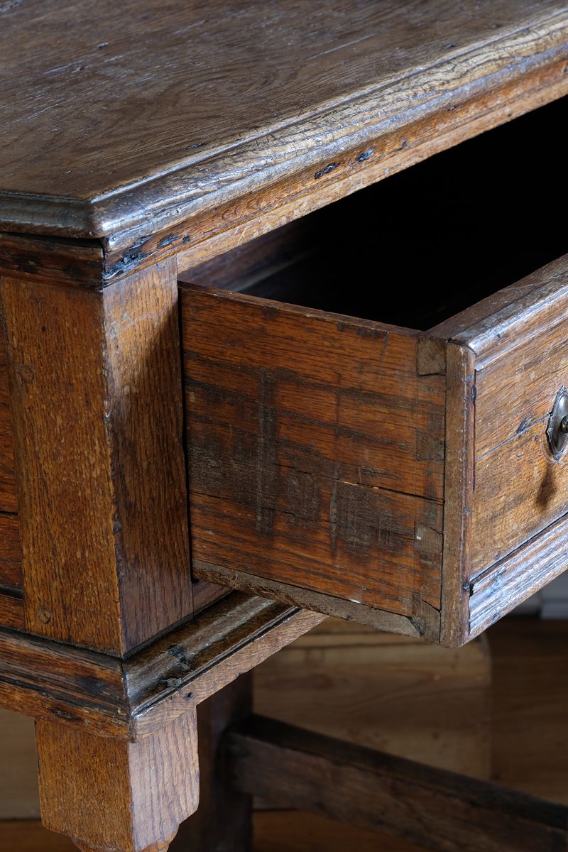 Close up of the hand cut dovetail joints on the 18th century country oak side table with a single panelled drawer, brass handles and baluster-turned front legs