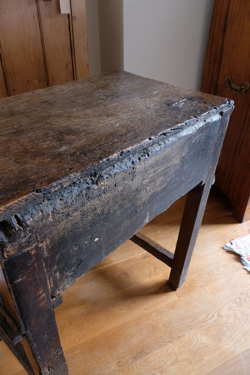 Rear photo showing the thick single board oak panel of the 18th century country oak side table with a single panelled drawer, brass handles and baluster-turned front legs